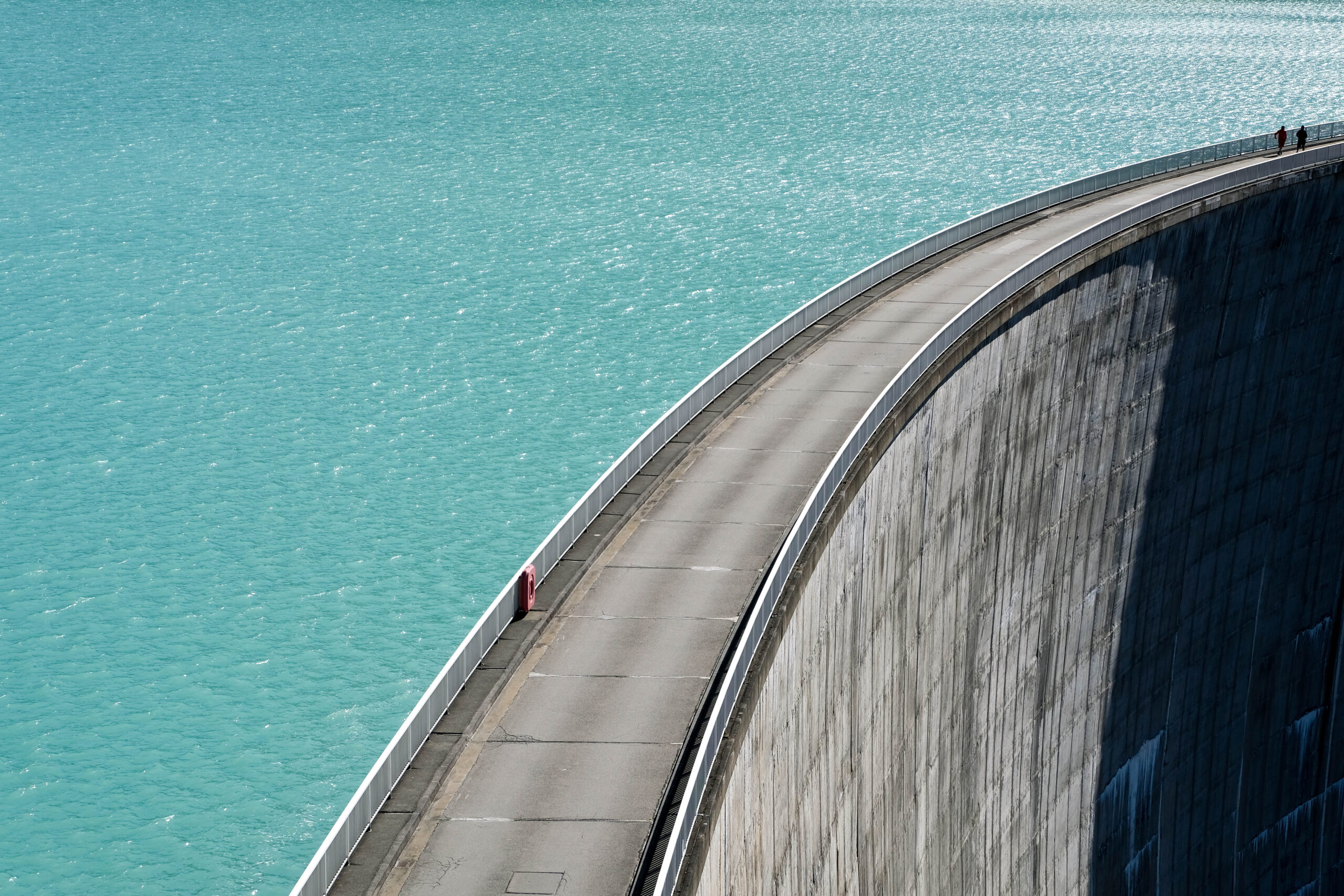 Hydroelectric power dam wall with water to the left and a sheer drop off to the right