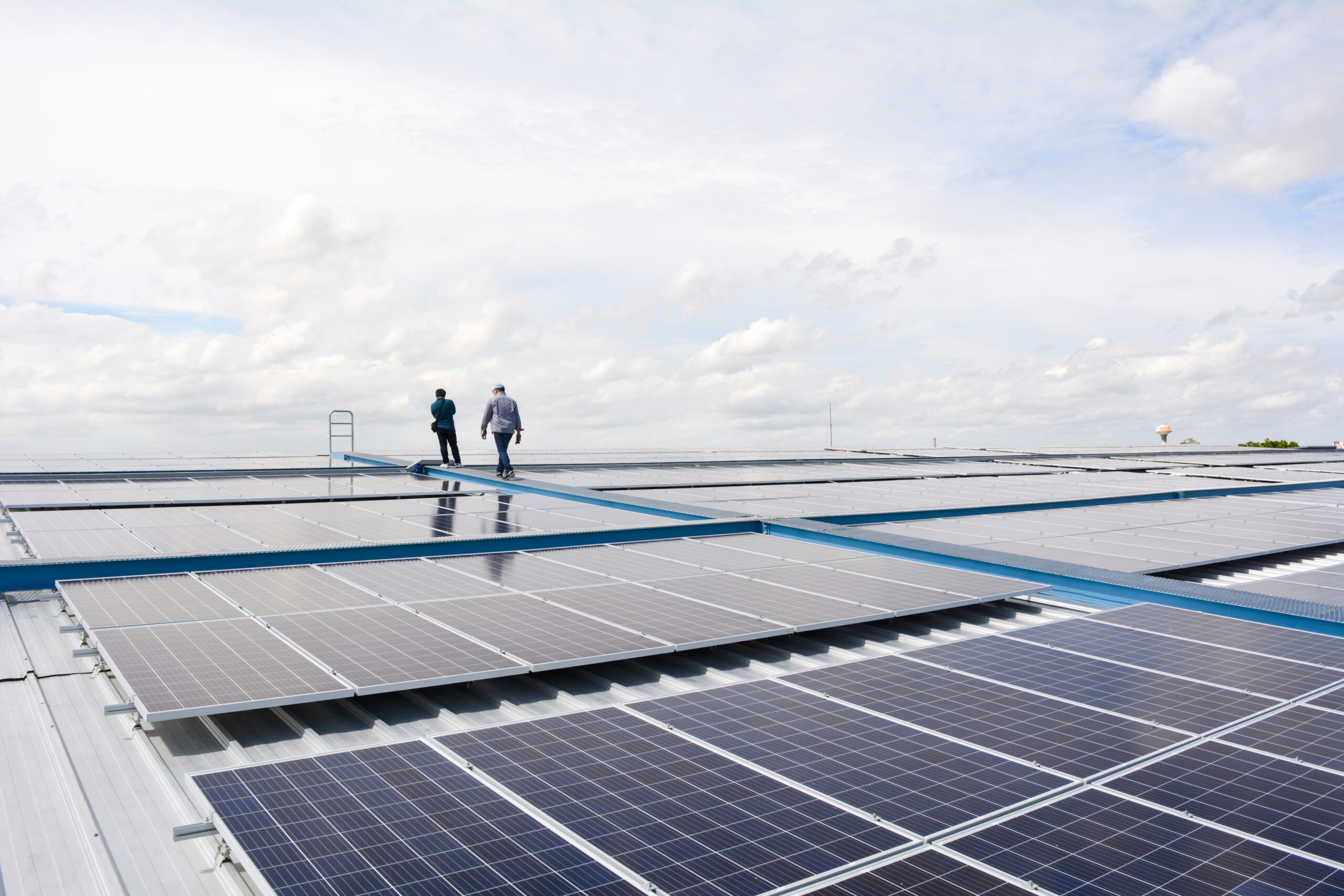 Close-up view of industrial rooftop solar panels with two men walking between the panel sets