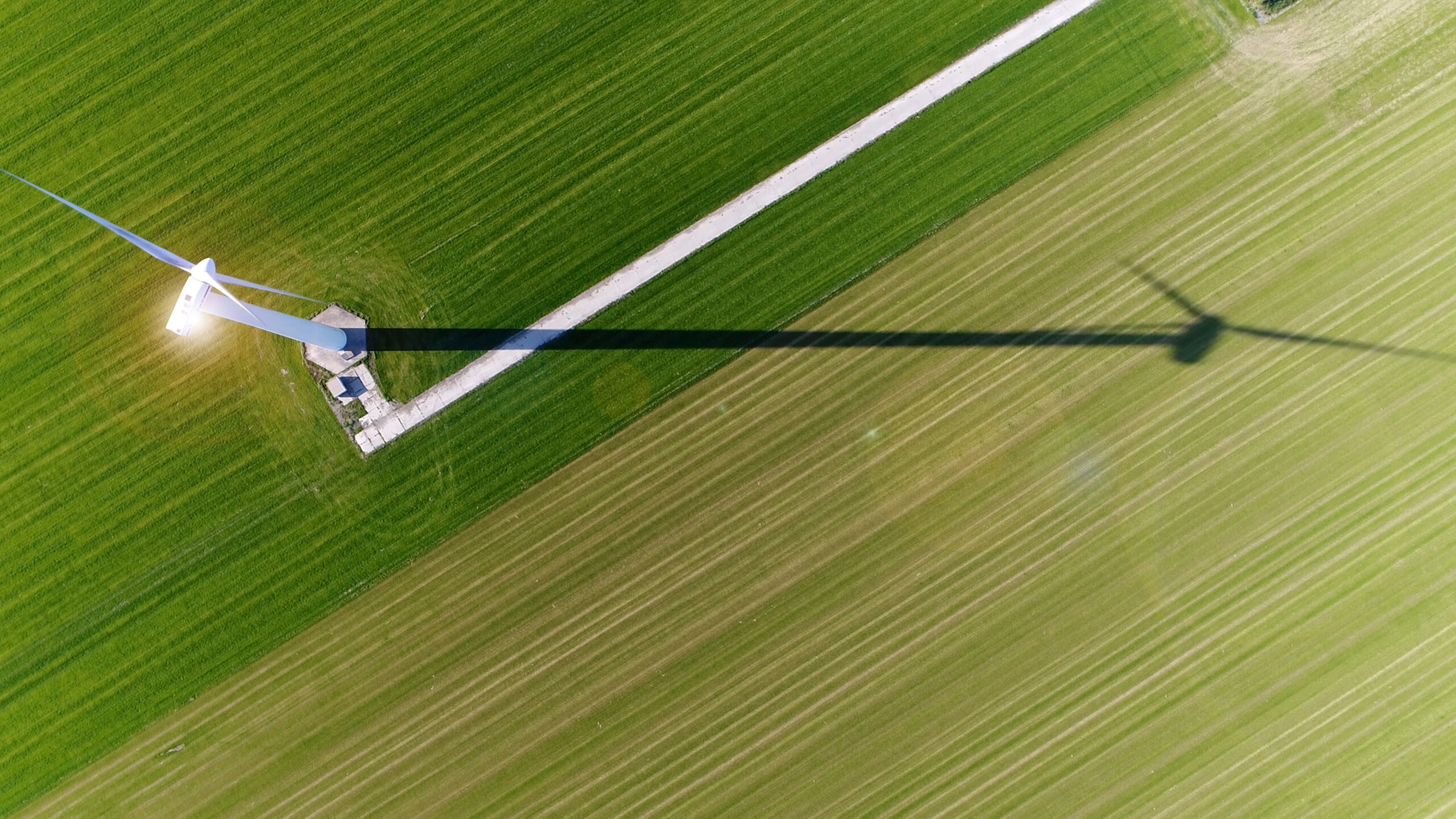 Aerial view of a wind turbine casting a long shadow on a piece of farmland