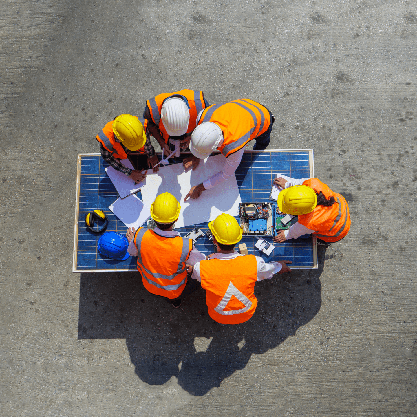 Top view of a group of engineers looking at blueprints spread on top of a photovoltaic solar panel at a construction site