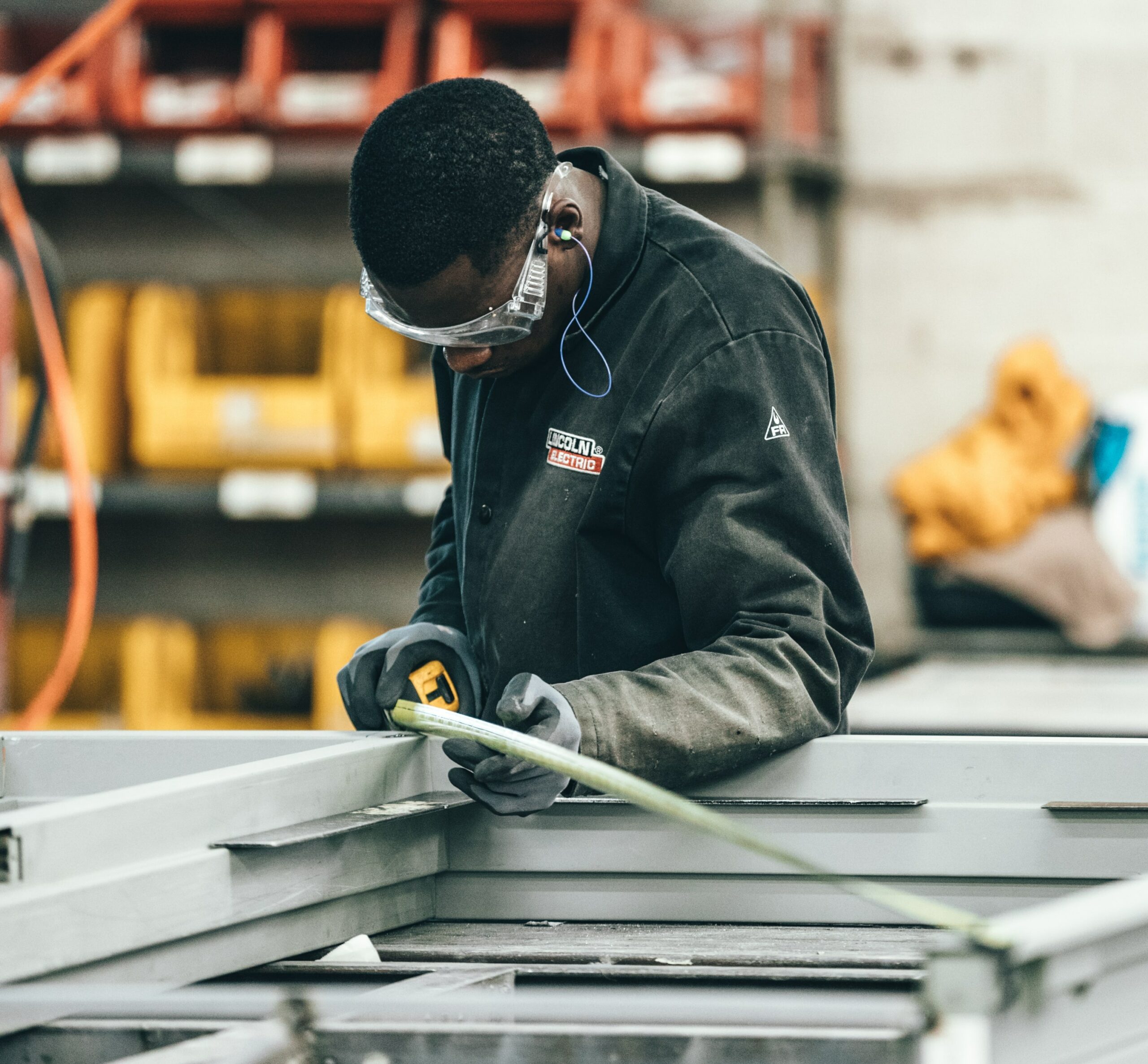 A factory worker wearing protective gloves and eyewear positioning a steel rod